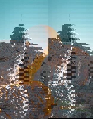 Ancient stone ruins with a historic mosque featuring a large dome in the background.