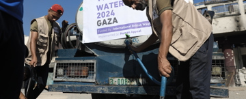 How to make a charitable waqf Aid workers distribute water from a tanker in Gaza, filling plastic containers. A banner reads "Water 2024 Gaza," indicating humanitarian support.