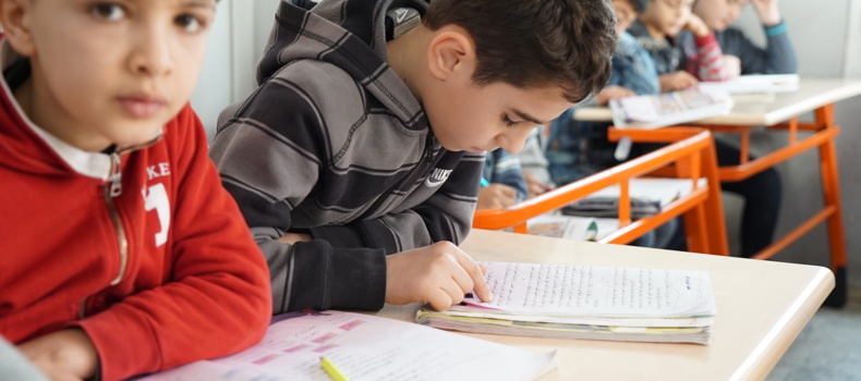 Students studying in a classroom, with one boy focusing on his notebook.