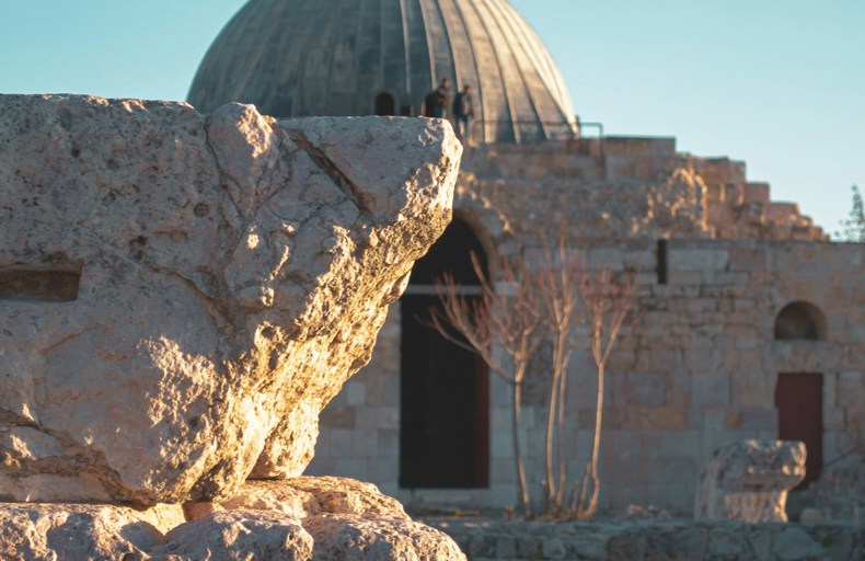 Ancient stone ruins with a historic mosque featuring a large dome in the background.