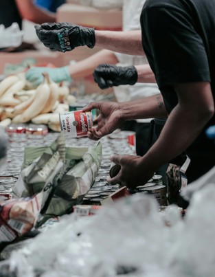 Ramadan Daily Sadaqah volunteers wearing gloves distribute canned goods and fresh produce at a food donation event.