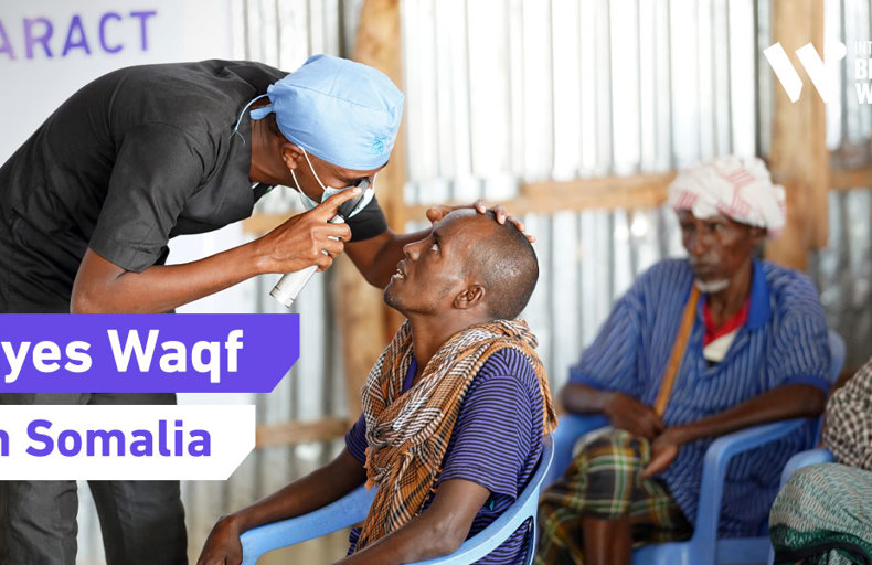 An eye doctor examines a patient at a medical camp in Somalia, with a banner reading "Eyes Waqf.